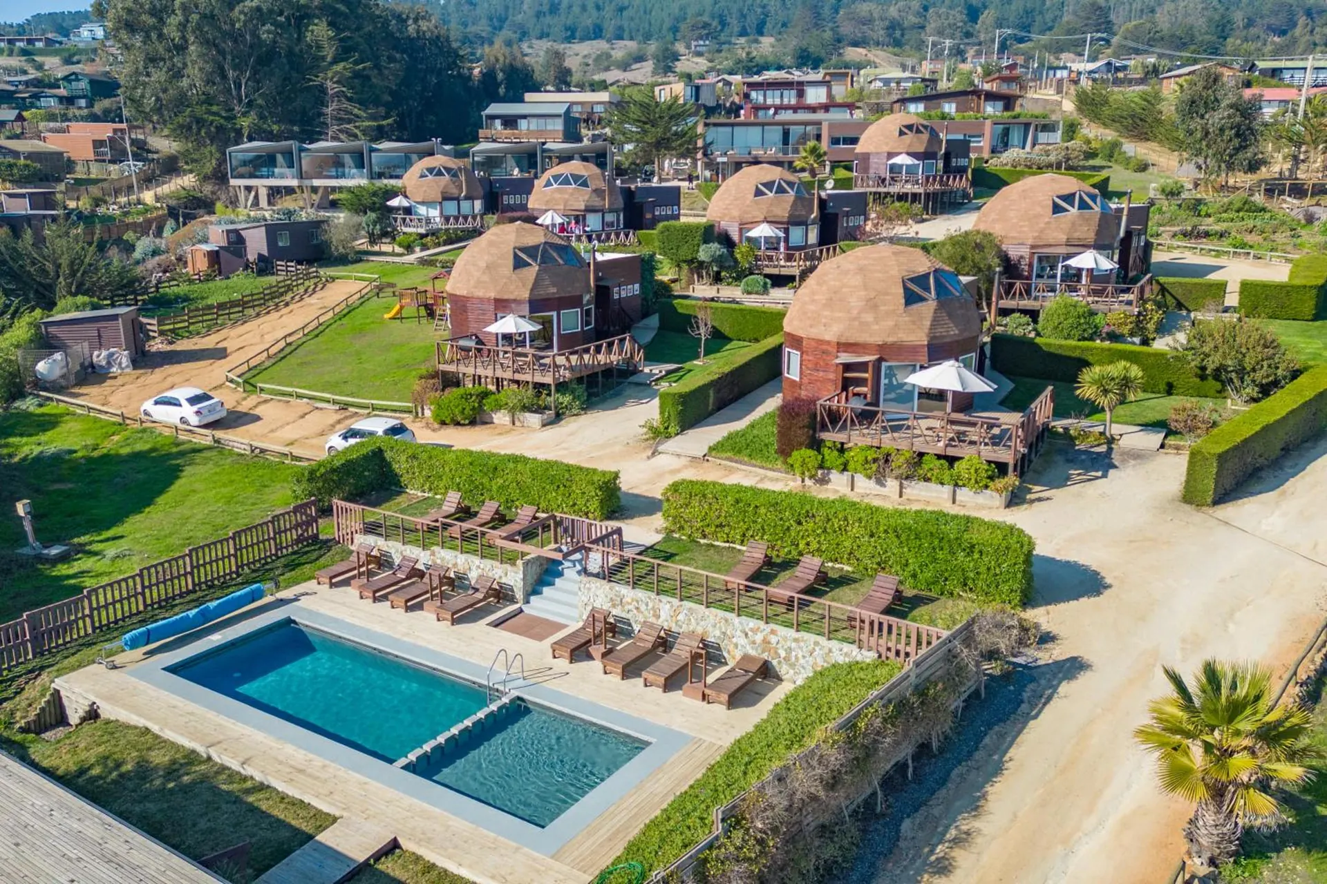 Aerial view of the domes and the cabins among gardens, with the pool and the loungers.