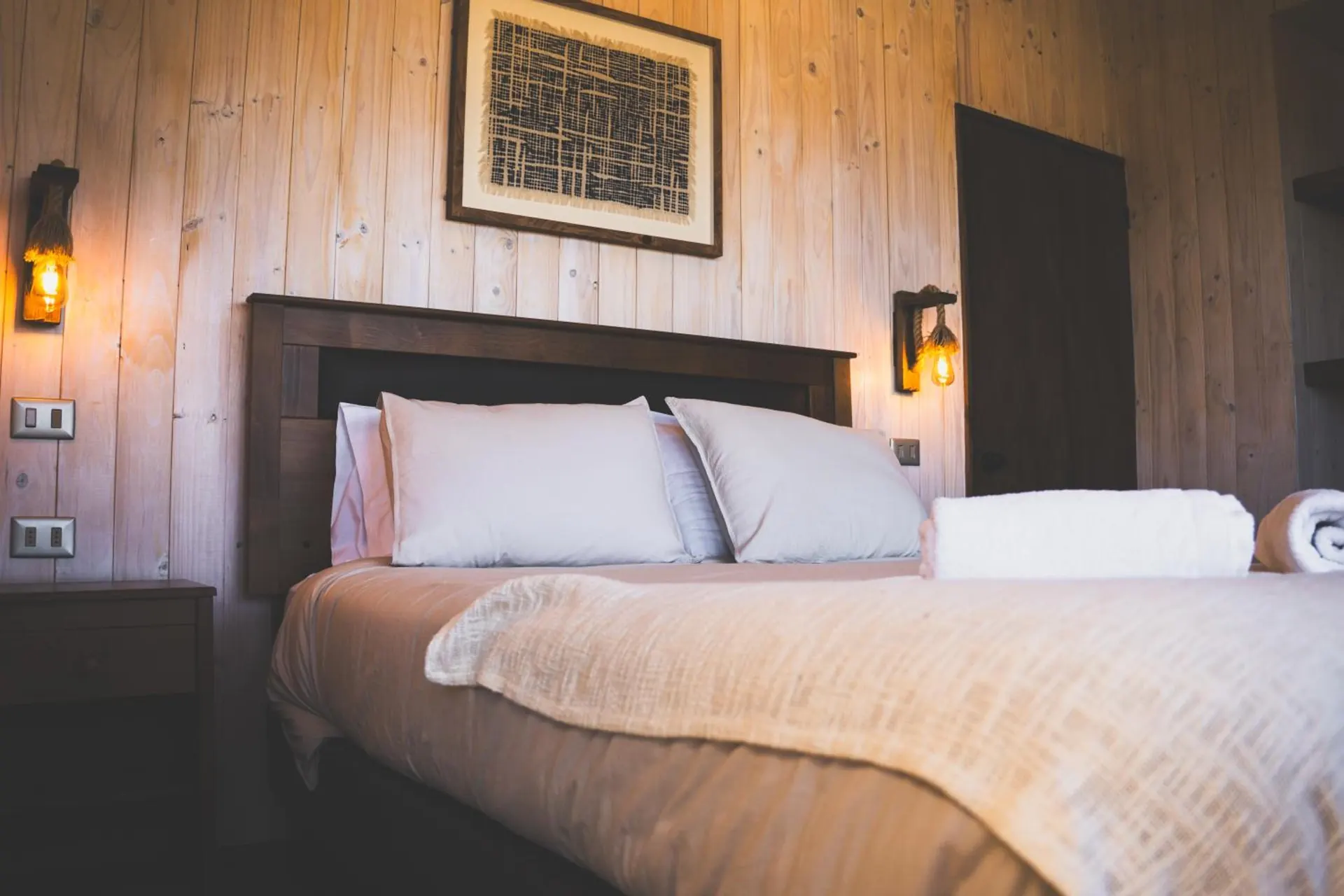 Cabin bedroom with a double bed, a wooden headboard, two lanterns and a picture.
