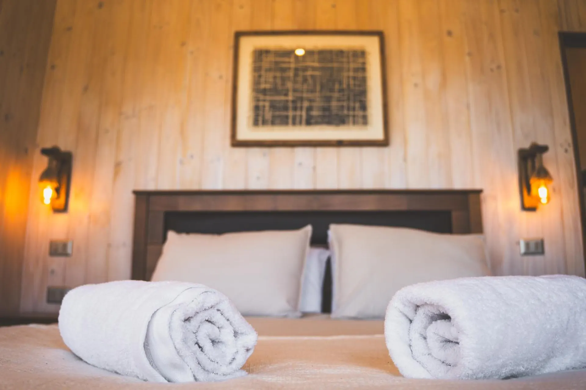 Double bed with rolled towels and two lanterns at the sides, on wooden walls.