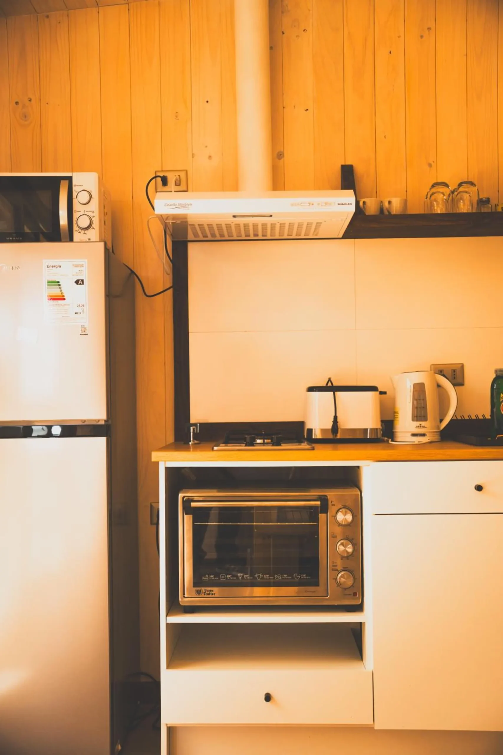 Kitchen of a cabin with a refrigerator, microwave, stove and utensils.