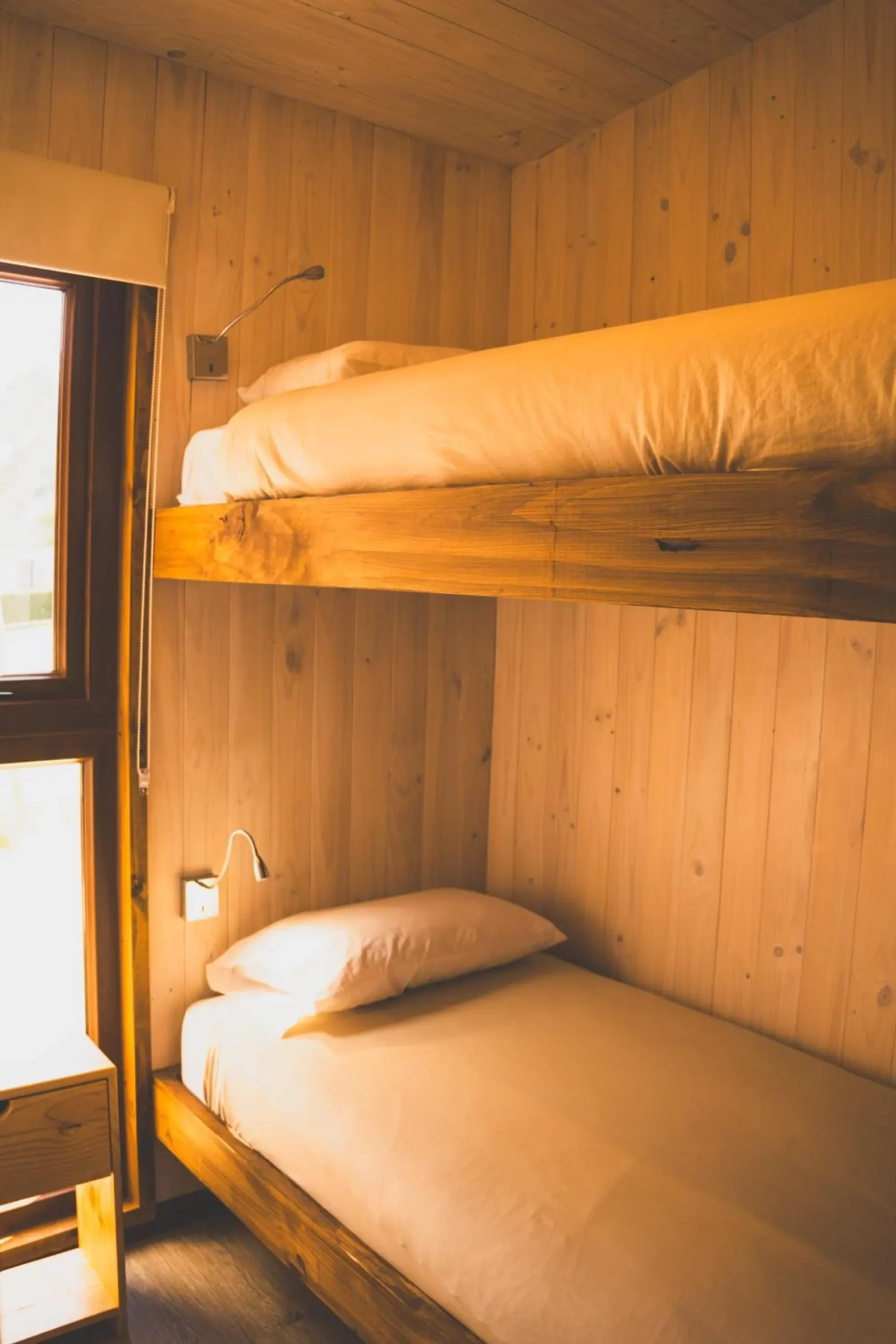 Wooden bunk bed next to a window, in a cabin bedroom.