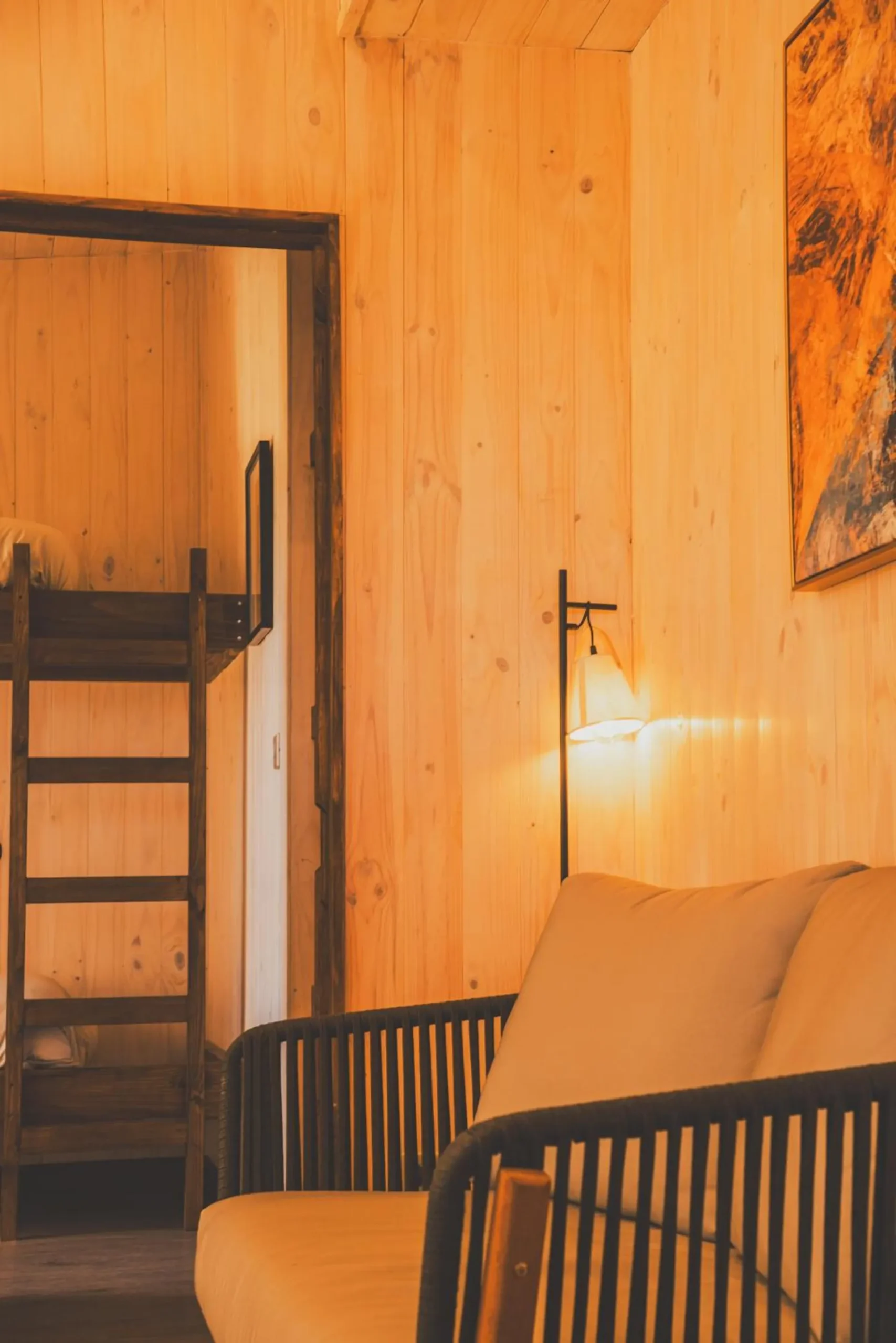 Corner of a cabin with a rattan chair, the staircase to a loft and wooden walls.