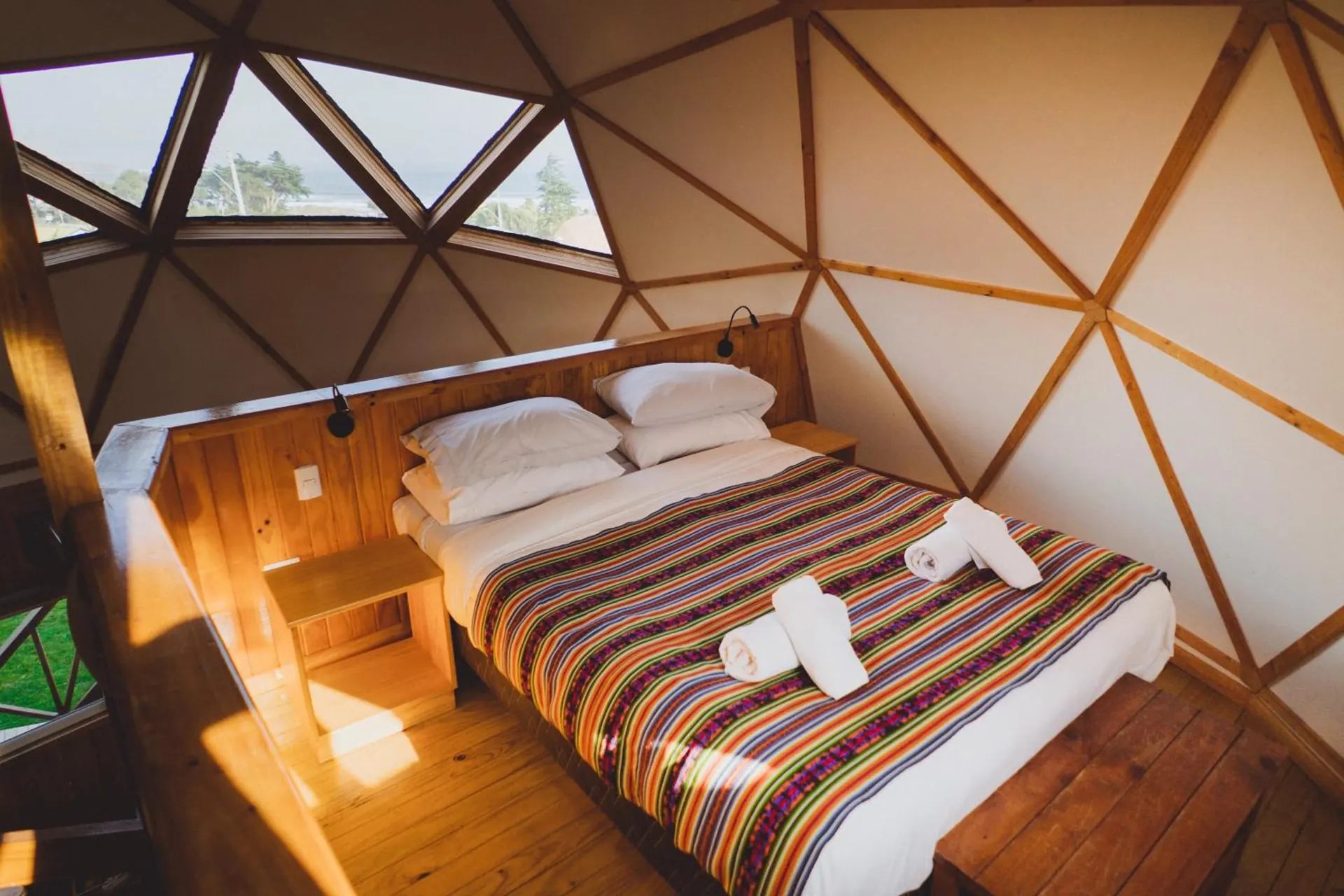 Bedroom of a dome with a double bed with a striped bedspread, under triangular windows.