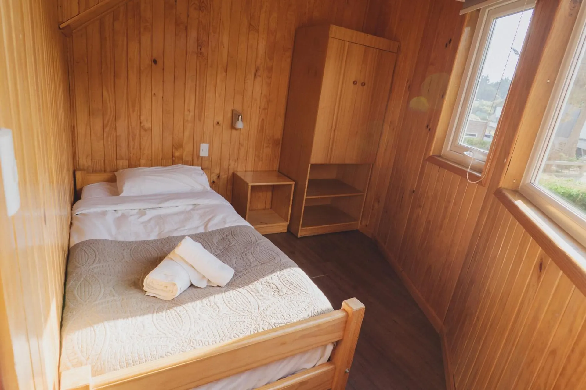 Bedroom with wooden walls, a double bed, folded towels and a wardrobe on the side.