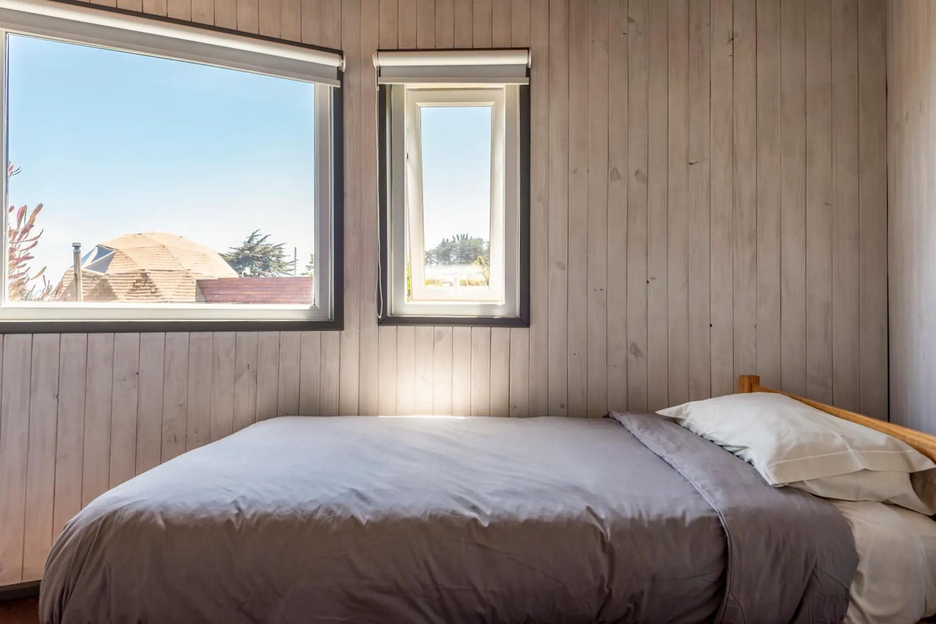 Wooden bedroom with a double bed under two windows, in daylight.