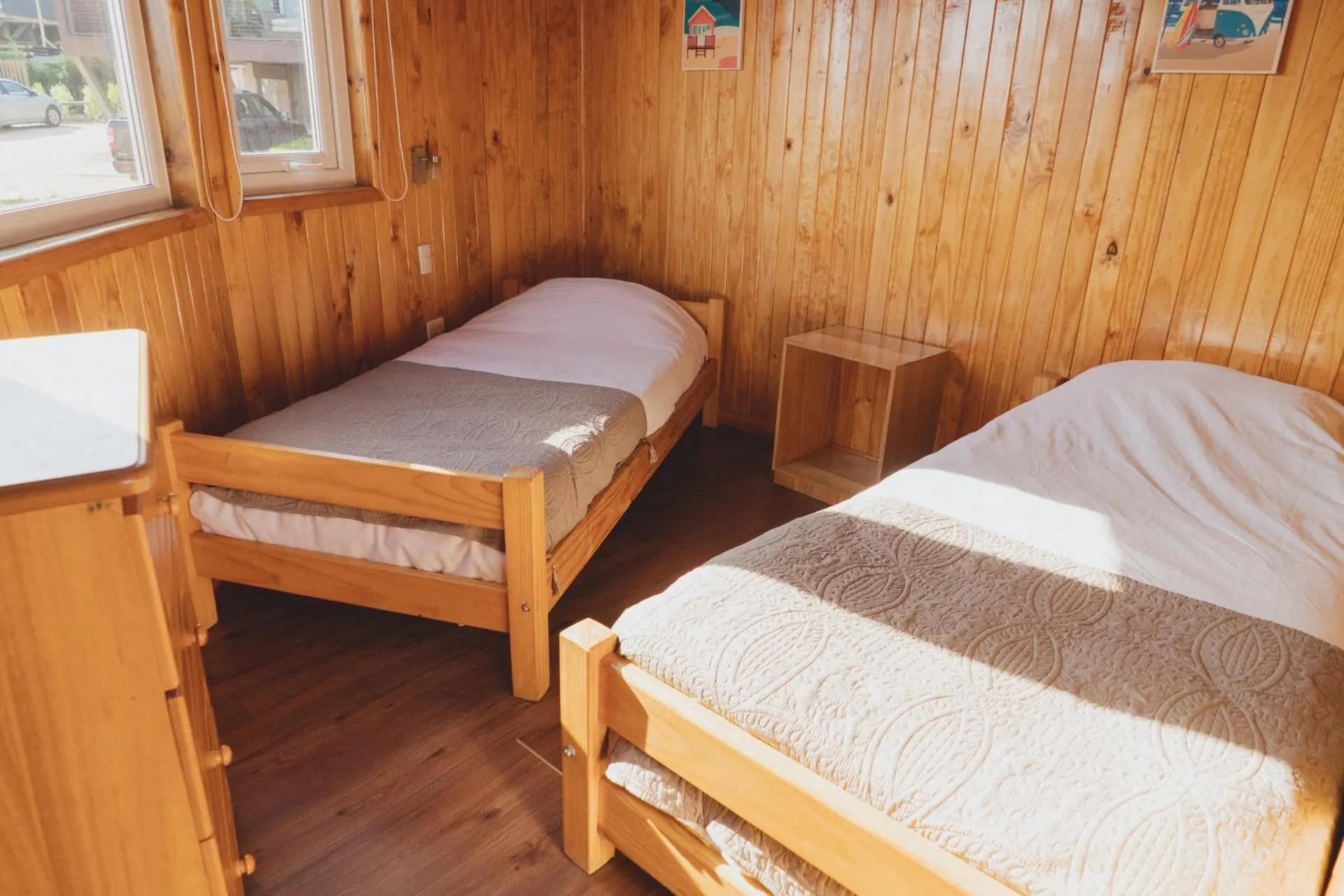 Bedroom with two single beds under a window, with wooden walls.