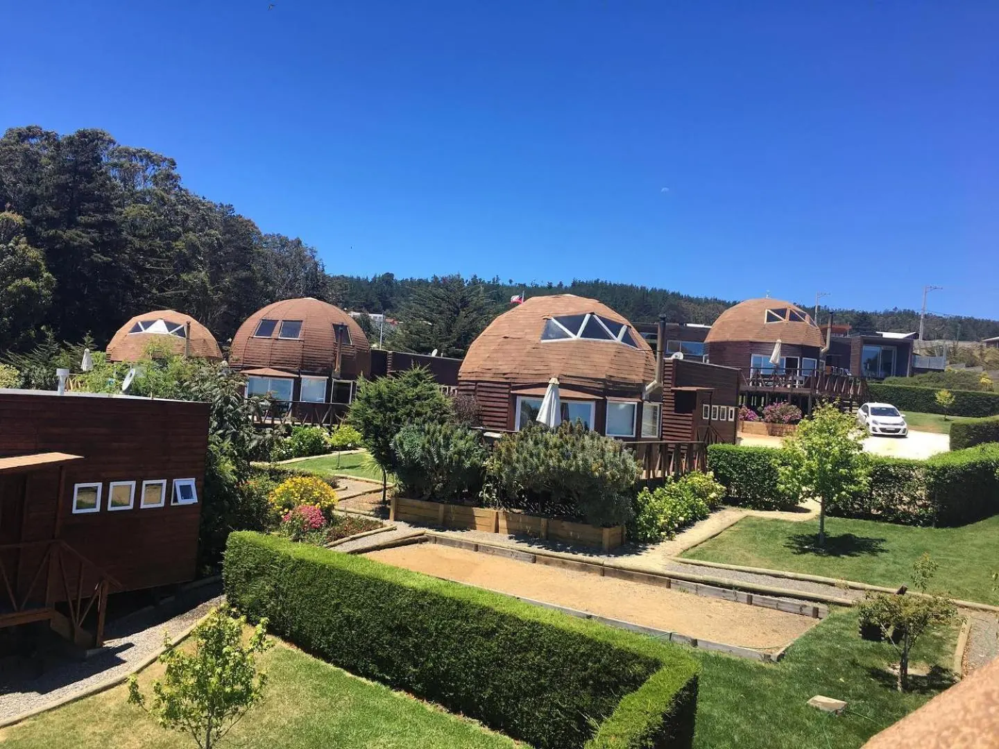 Wooden domes among gardens with living fences, under a blue sky.