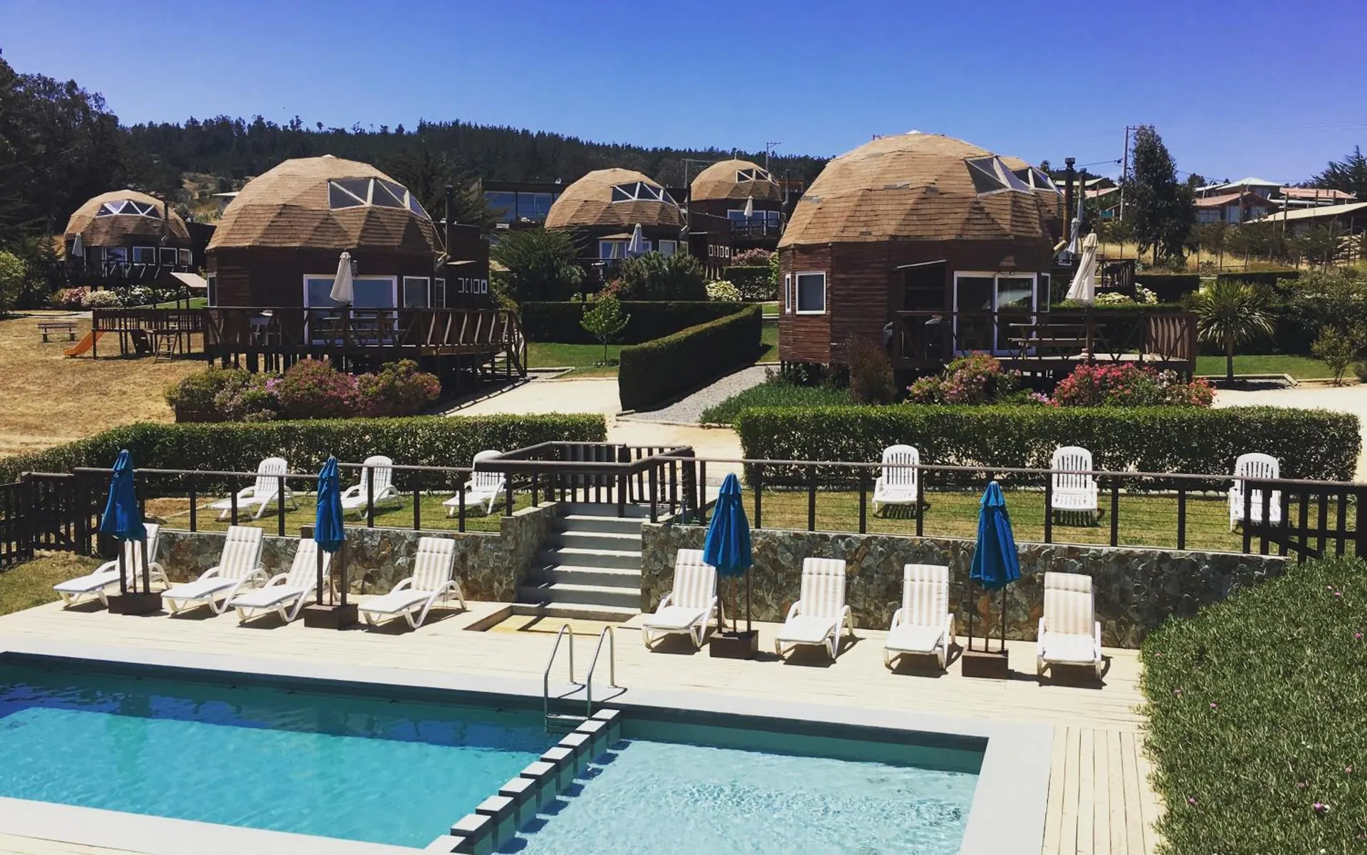 The pool with a ladder, white loungers and blue parasols, with the domes behind.
