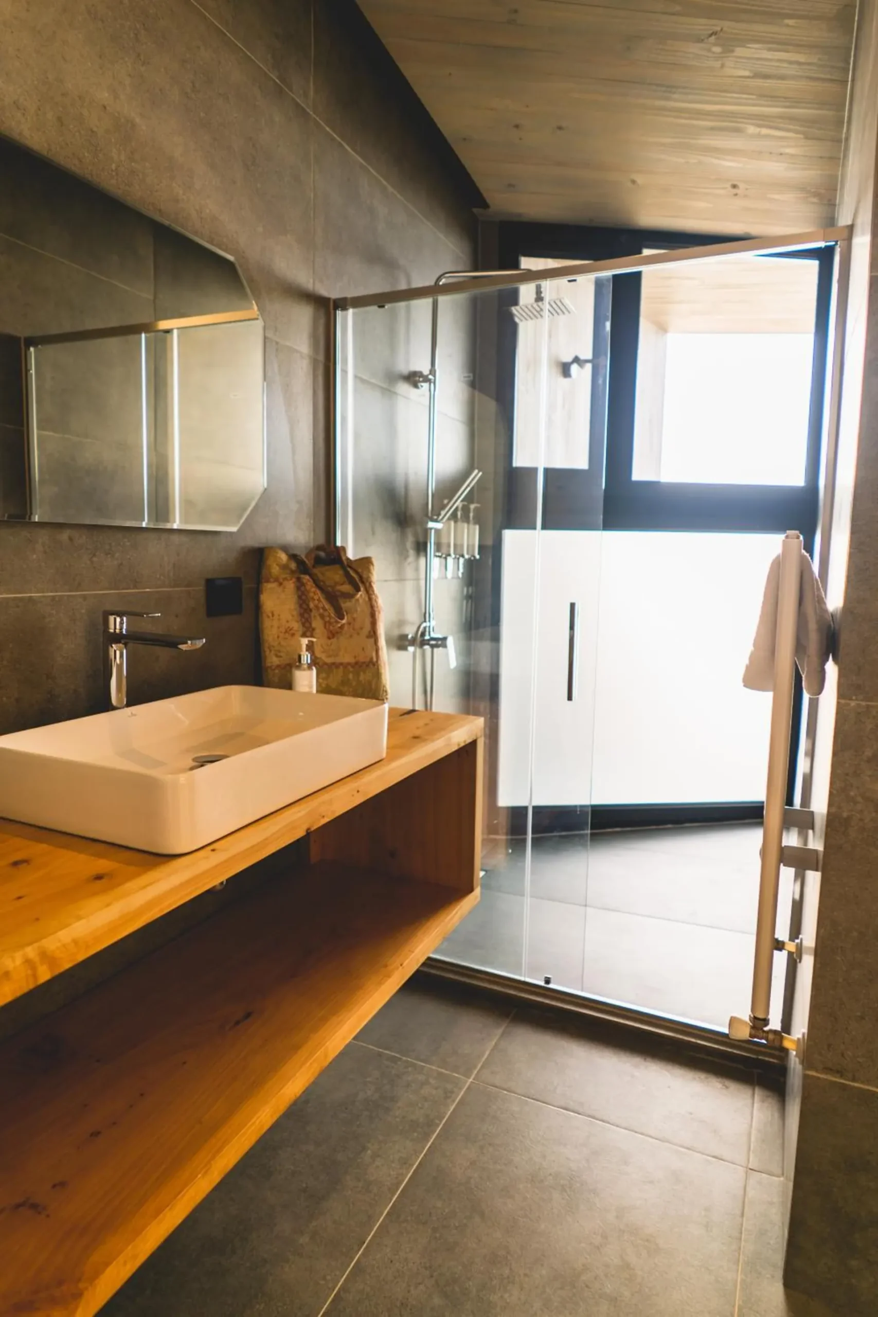 Bathroom of a suite with a glass shower, a wooden washbasin and a concrete floor.