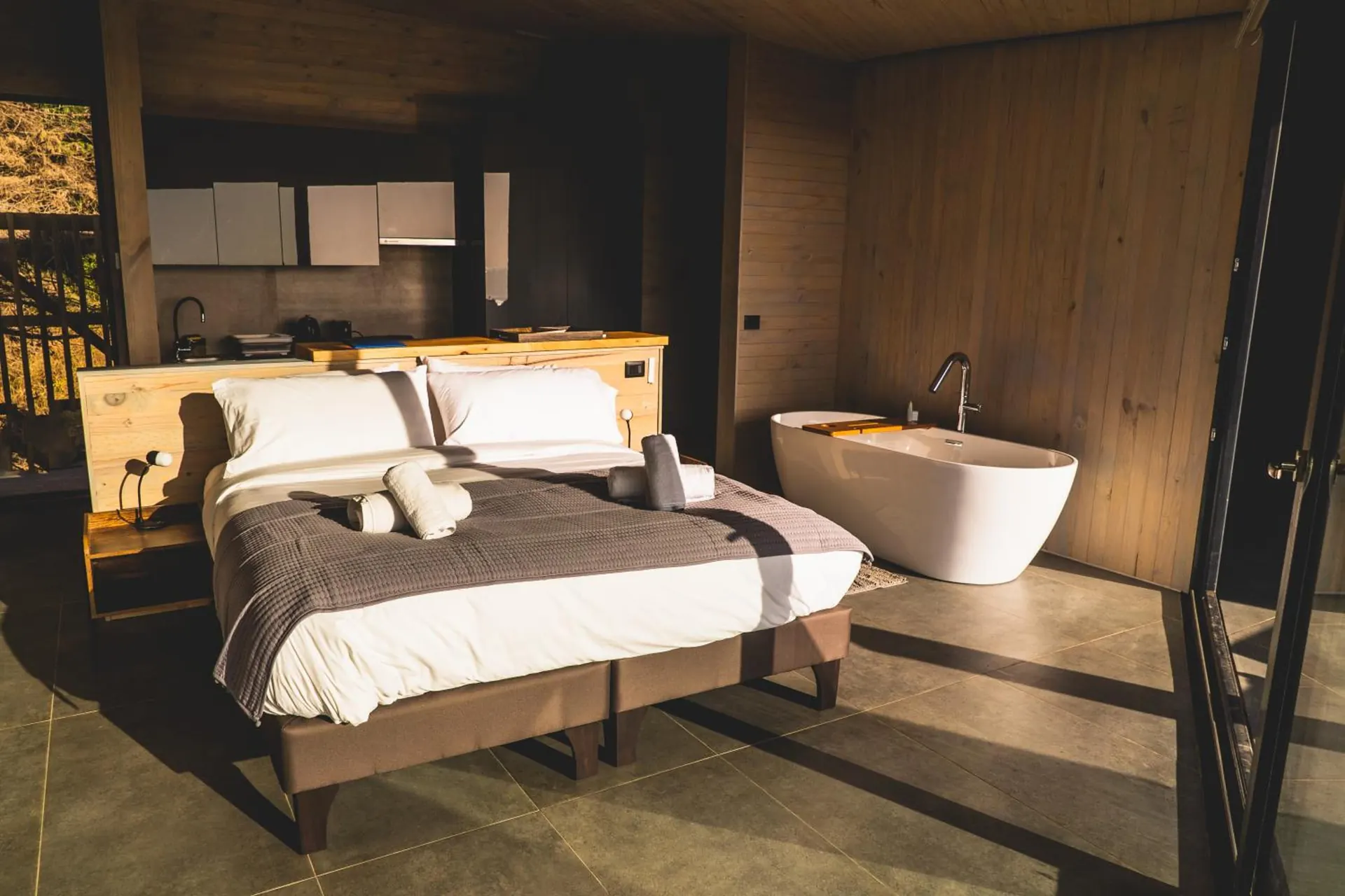 Suite de madera y concreto con cama doble, bañera exenta y cocina equipada.
