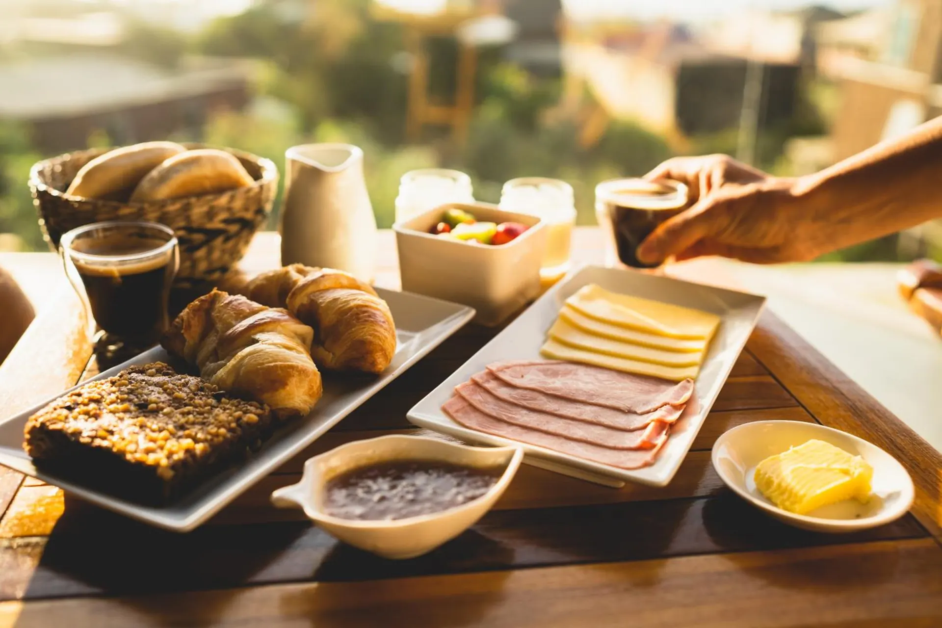 Bandeja de café da manhã com pão, torradas, frios, manteiga e café sobre a mesa.