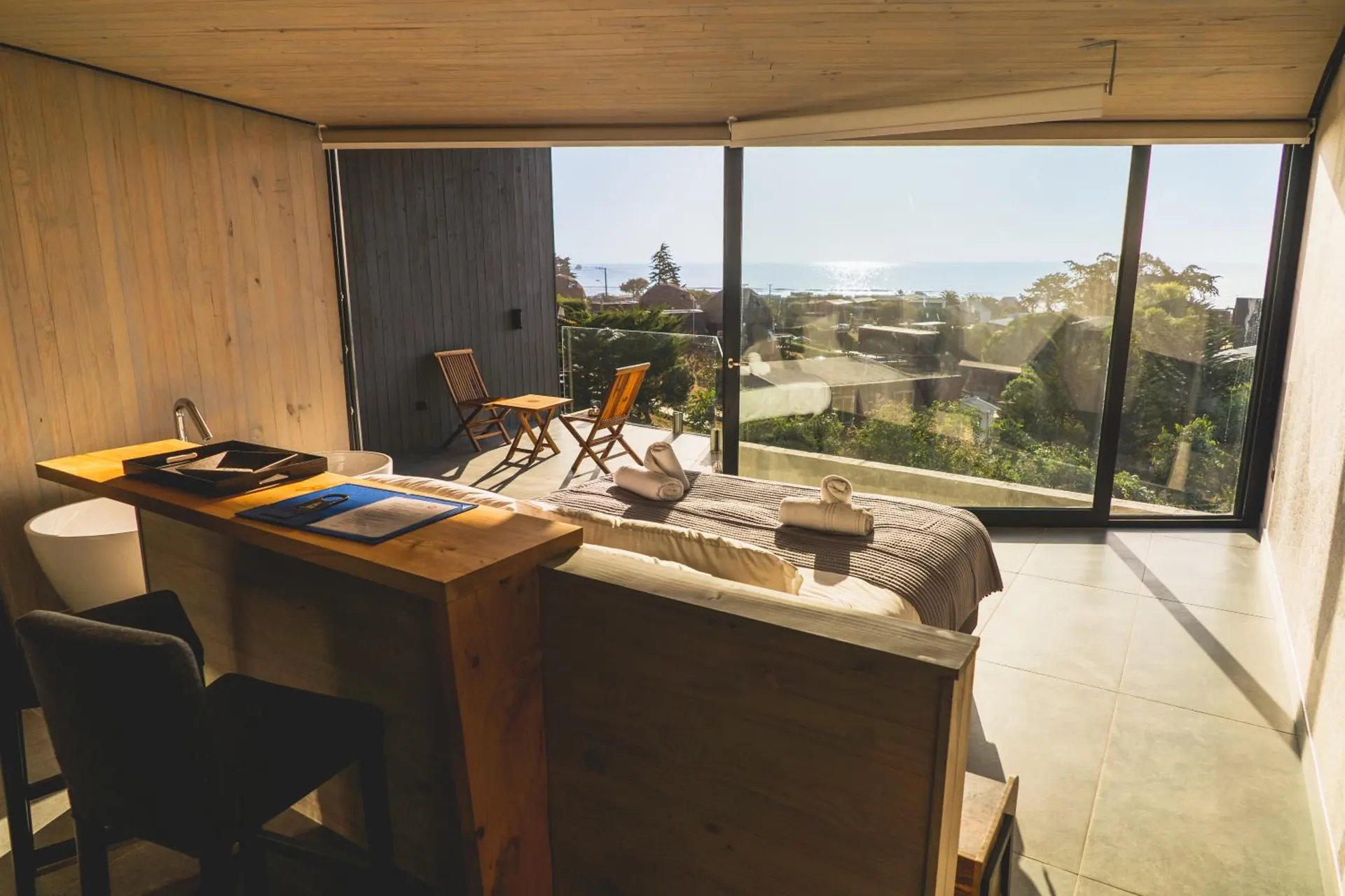 Suite with a large window looking at the sea, a work table and the bed in the back.