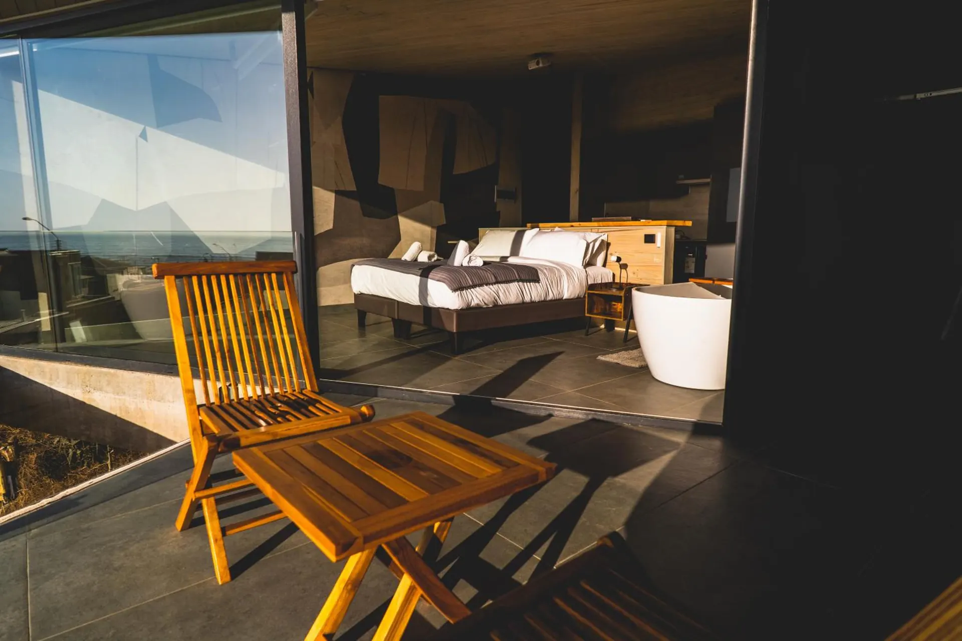 Wooden chair and small table on the terrace of a suite, with the bed in the back.