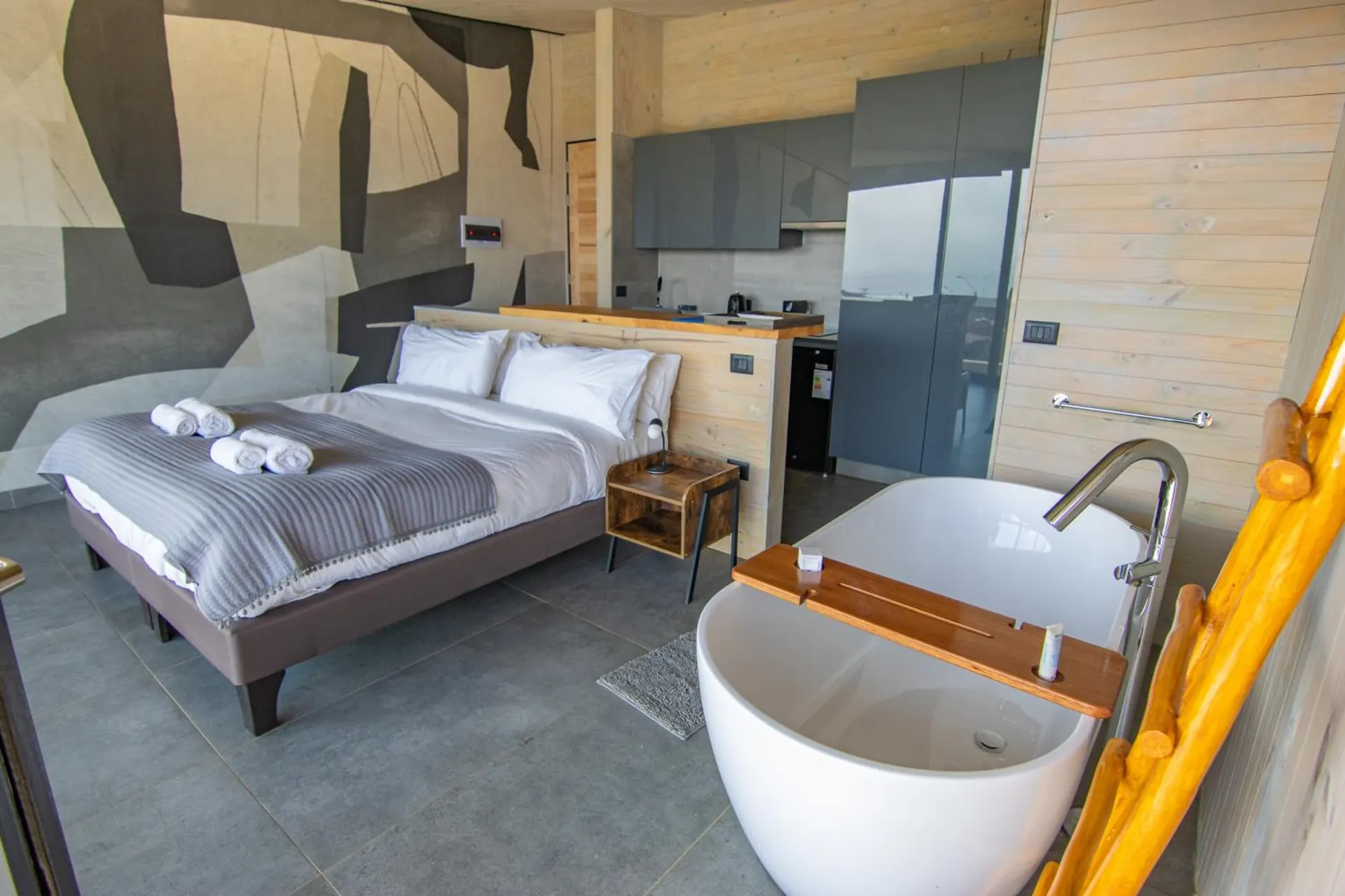 Suite with a double bed, a freestanding tub next to the bed and a kitchen in the back.