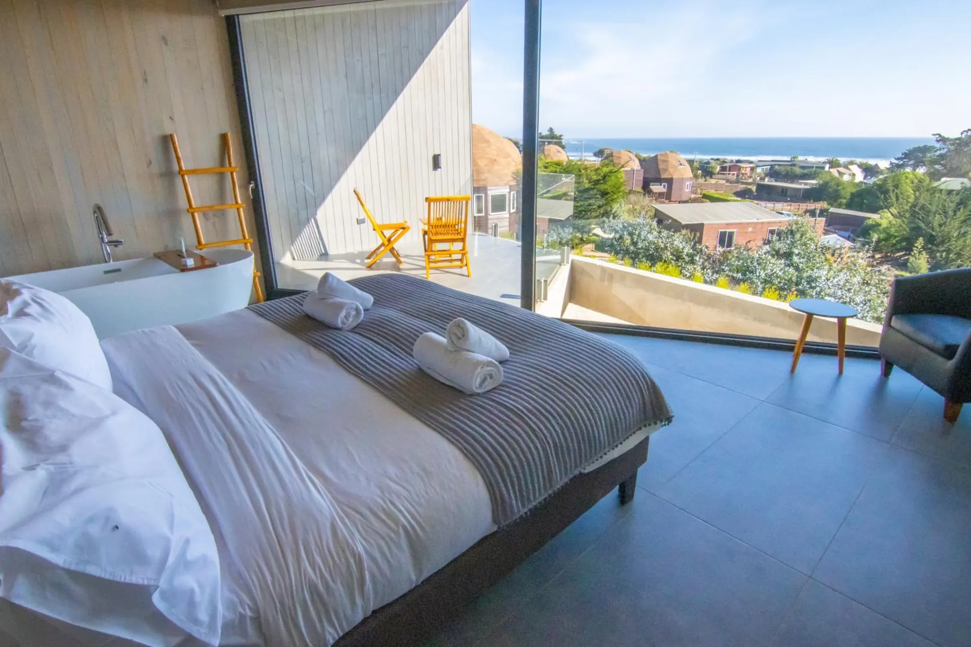 Cama doble con cubrecama gris frente a un ventanal con vista al jardín y los domos.