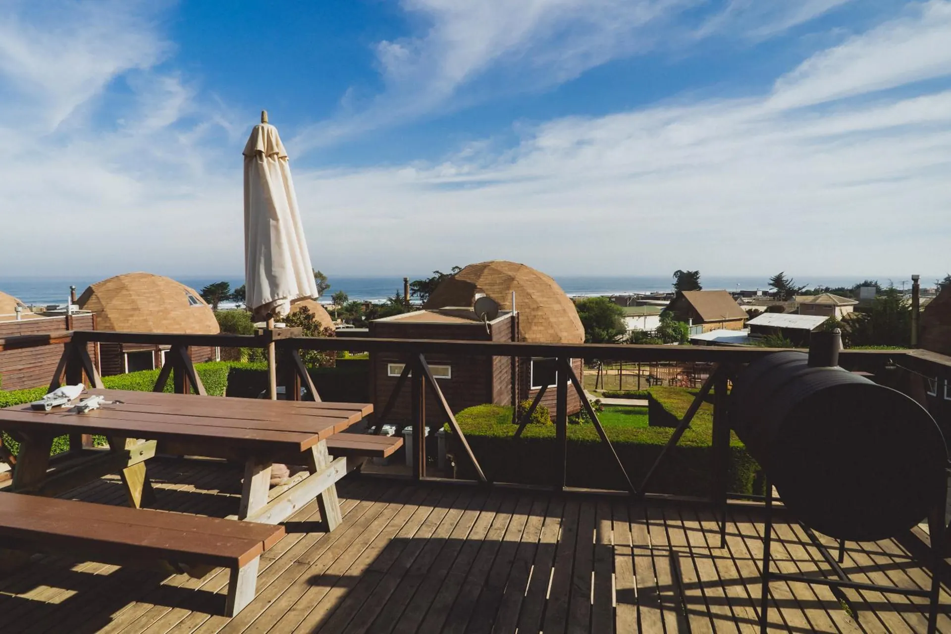 Wooden terrace with a picnic table, a parasol and the sea in the background, among domes.